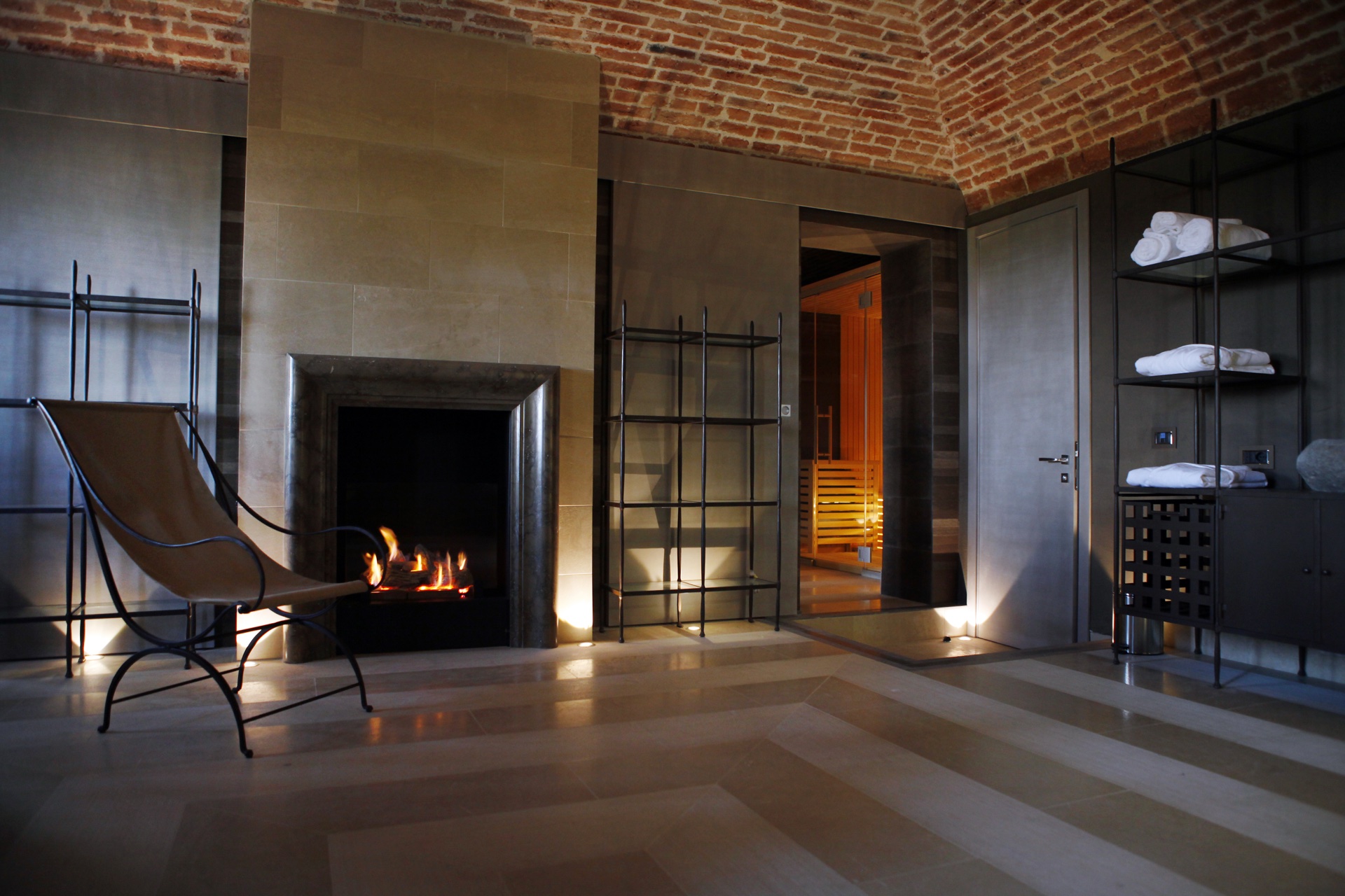 La SPA della Torre dei Canonici con camino acceso, chaise longue in ferro, soffitto a volta in mattoni a vista e sauna finlandese sullo sfondo