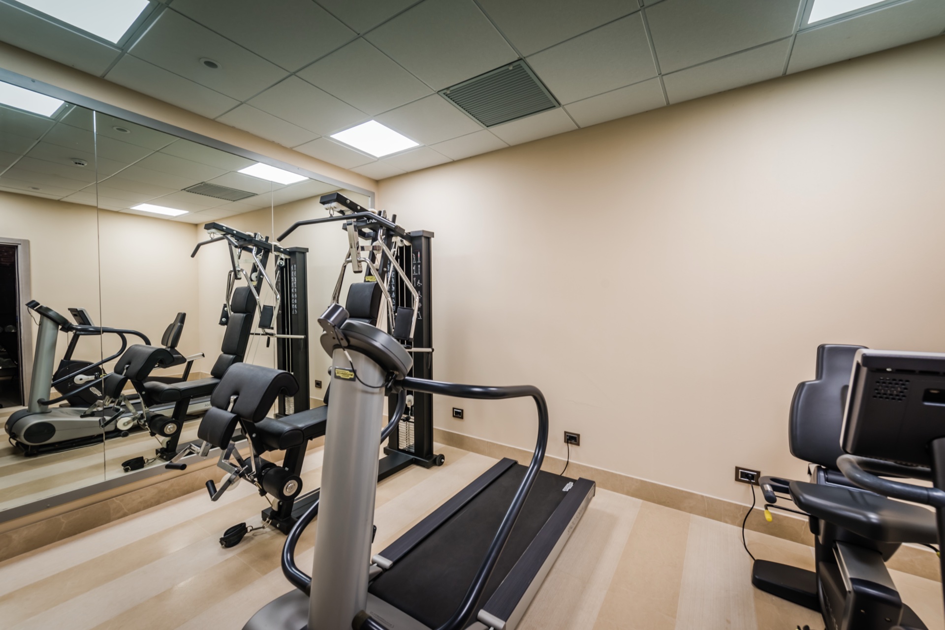 Sala fitness della Torre dei Canonici con macchina multifunzione Technogym, tapis roulant e specchio a parete