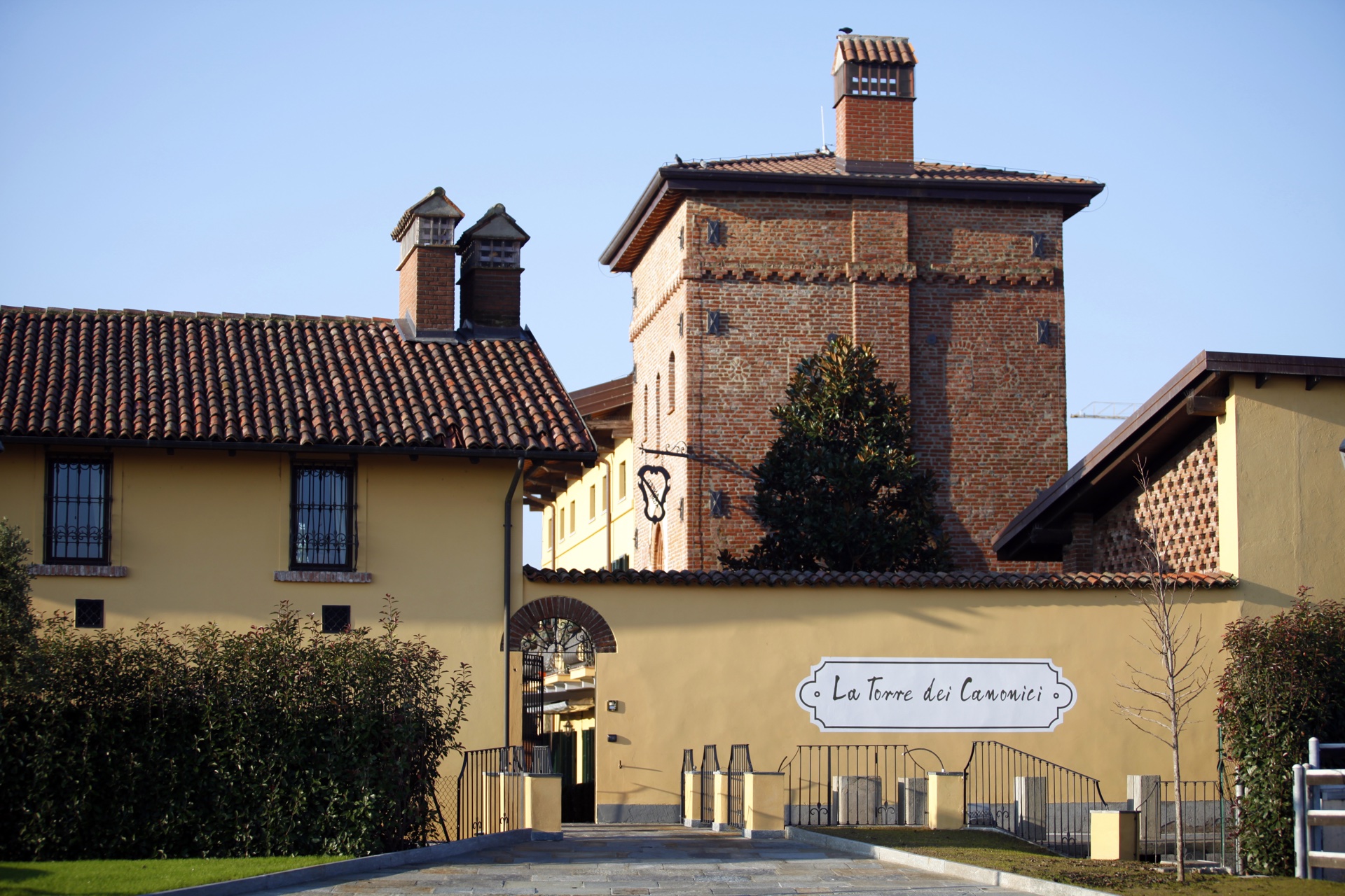 La Torre dei Canonici vista dal vialetto d’ingresso: la torre medievale in mattoni, il corpo padronale con l’insegna e la corte interna
